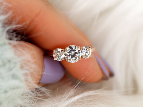 Three-stone moissanite ring held between fingers with a soft background