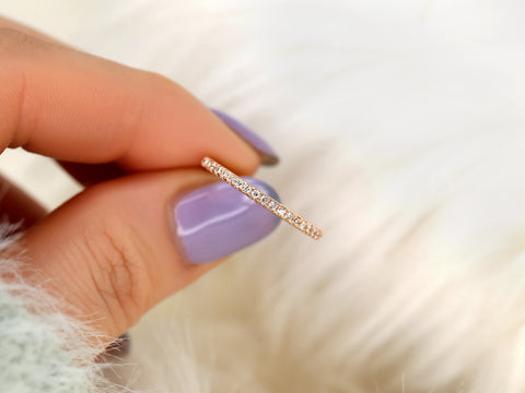 Gold ring being held by a hand with purple nail polish on a soft white background
