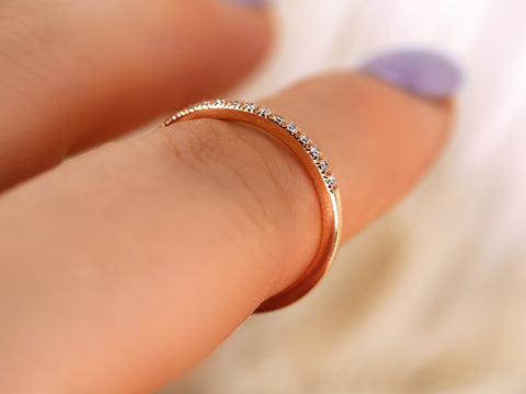 Rose gold ring with small diamonds on a finger against a blurred background