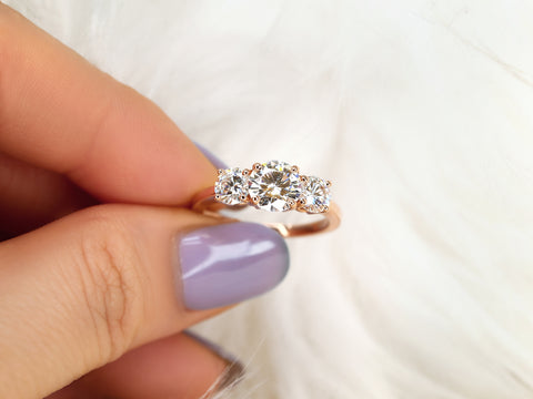 Close-up of a hand wearing a three-stone moissanite ring by pinched fingers