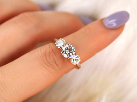 Close-up of a hand wearing a three-stone moissanite ring with a blurred background