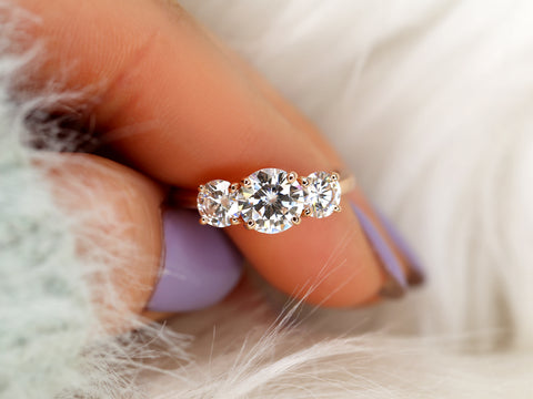Three-stone moissanite ring held between fingers with a soft background