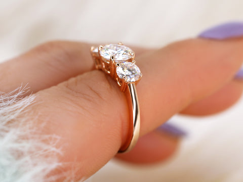 Rose gold ring with three moissanites on a finger against a blurred background