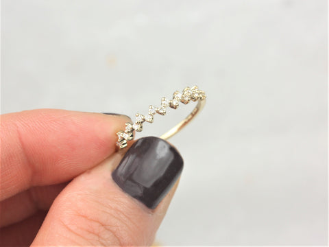 Hand holding delicate 14kt gold ring with diamonds set halfway around band on light neutral background