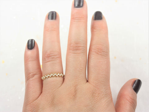 Hand wearing a delicate 14kt gold halfway eternity ring with small diamonds on a light background