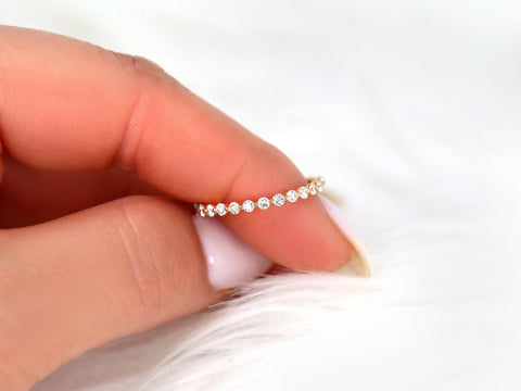 Rose gold delicate ring with small sparkling diamonds set almost entirely around the band held against soft white background