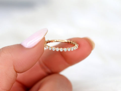 Delicate rose gold ring with small sparkling diamonds in a half-eternity style held between thumb and finger