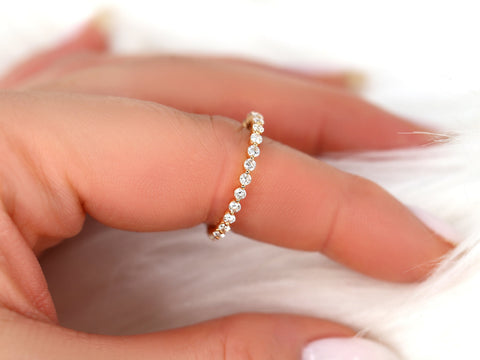 Close-up of delicate rose gold ring with small sparkling diamonds held between fingers on soft white background