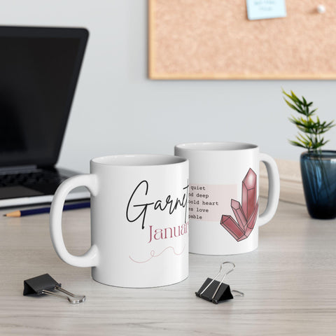 Two white ceramic mugs with garnet crystal illustration and elegant script text on a light wood office desk