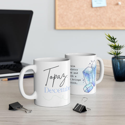 Pair of white mugs featuring December birthstone design with blue crystal illustration and script text on a desk