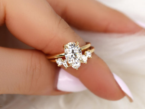 Oval moissanite engagement ring paired with a curved gold band featuring three smaller sparkling stones, held by hand.