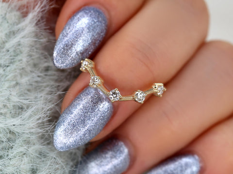 Gold ring with five bezel-set diamonds arranged in a delicate curved design on a hand with silver glitter nails