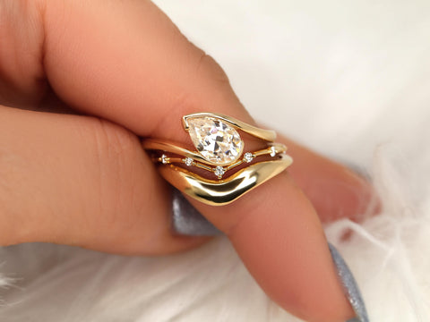 Close-up of a 14kt gold tilted pear moissanite solitaire bridal ring set with delicate accent stones on finger