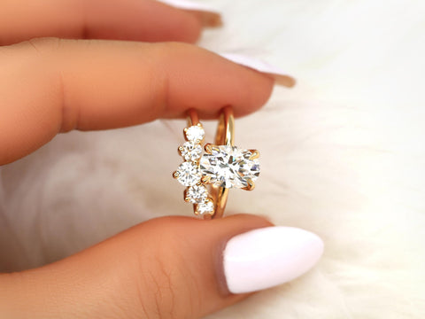 Hand holding two 14kt gold rings, one featuring an oval solitaire moissanite and the other with three round stones bridal set