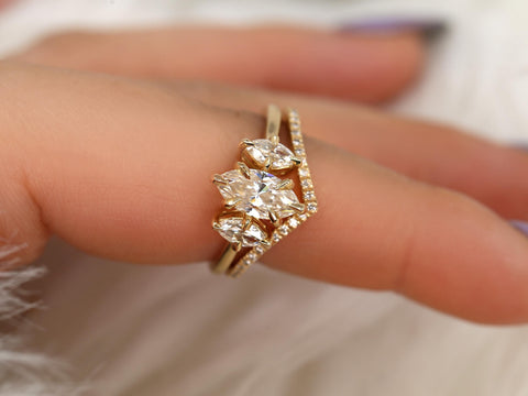 Close-up of a hand wearing a moissanite marquise three-stone engagement ring with a curved diamond-accented gold band