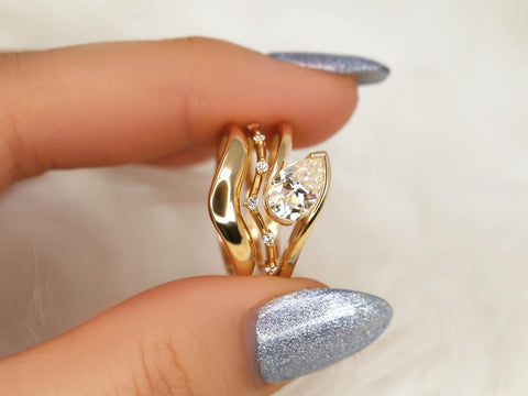 Set of three 14kt gold rings featuring a tilted pear-shaped moissanite solitaire and delicate accent stones bridal set
