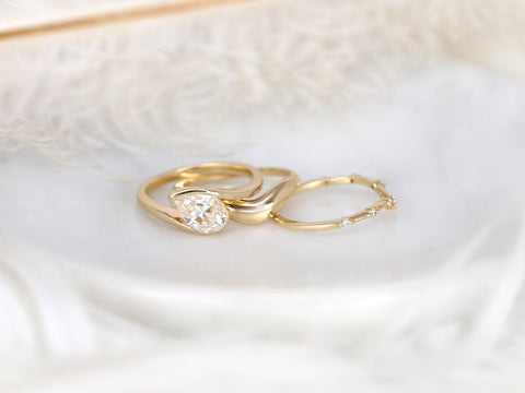 Three delicate gold rings including a tilted pear-shaped moissanite engagement ring with matching curved and diamond-accented bands