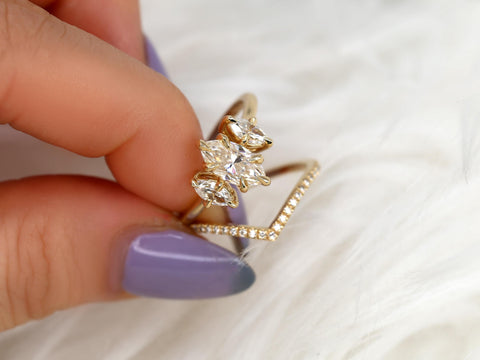 Close-up of a hand holding a marquise three-stone moissanite bridal set with a diamond-accented chevron band