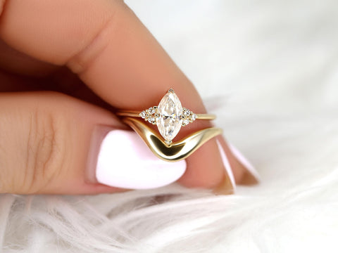 Close-up of a hand holding a gold moissanite marquise cluster engagement ring paired with a curved wedding band