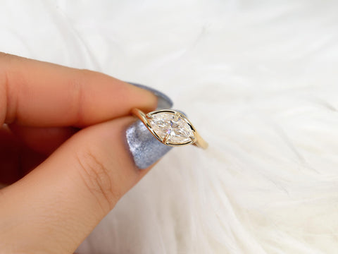 Hand holding a gold ring with an east-west marquise diamond solitaire on a soft white background