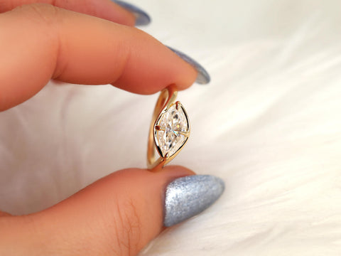 Close-up of a hand with silver nail polish holding a gold band ring featuring a horizontal marquise diamond solitaire design.