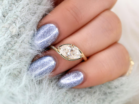 Hand displaying a marquise-shaped diamond solitaire set horizontally on a sleek gold band, ideal for engagement or milestone gifts