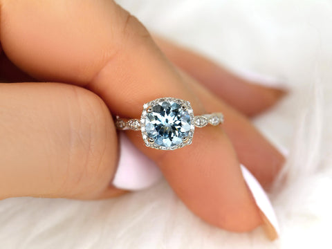 Close-up of a hand holding an 8mm aquamarine diamond ring with milgrain detailing and diamond halo on a delicate band