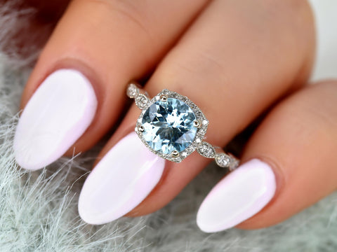 Close-up of a hand with pale pink nails wearing an 8mm aquamarine diamond ring with milgrain cushion halo and diamond accents