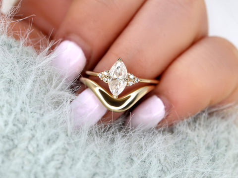 Hand holding a marquise moissanite engagement ring with a curved gold wedding band, fine bridal set jewelry.