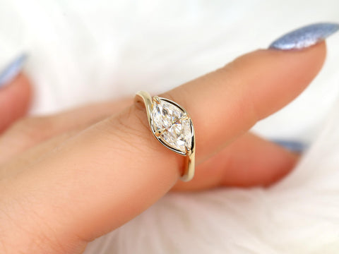 Hand wearing a gold ring with a horizontally set marquise diamond on a soft white background, fine jewelry design.