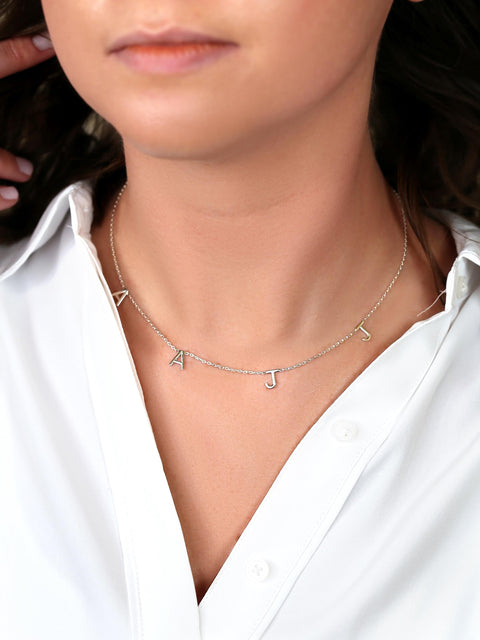 Necklace with letter 'A' and 'J' charms worn by a person in a white shirt.