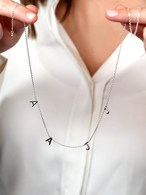 Person holding two silver necklaces with letter pendants against a white background