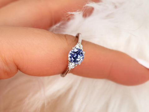 cornflower blue sapphire trilogy ring on pointer finger and white background