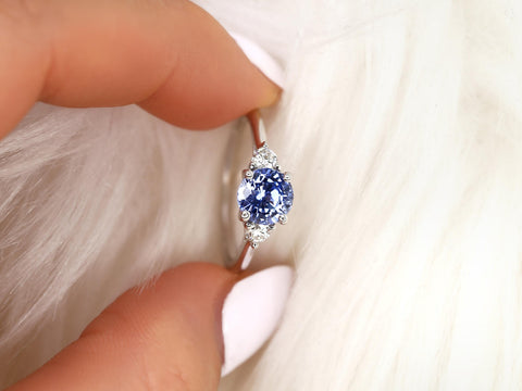 cornflower blue sapphire three stone ring between two fingers on white background