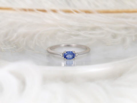 oval cornflower blue sapphire ring in trilogy style with two diamonds on white gold front view on white background with feathers