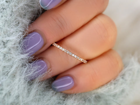 Close-up of a hand with purple nail polish wearing a gold ring on a soft, gray background