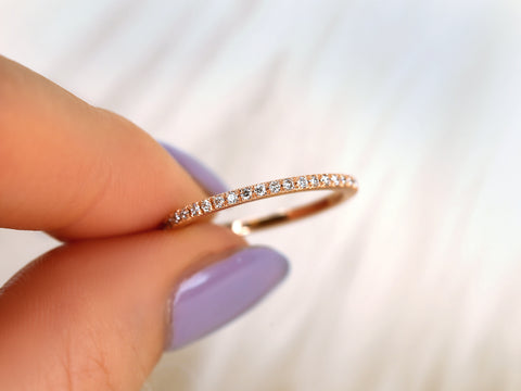 Rose gold ring with diamonds held between fingers against a blurred background
