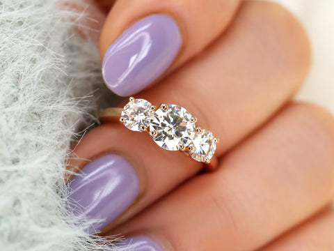 Close-up of a hand wearing a three-stone moissanite ring with lavender nail polish.