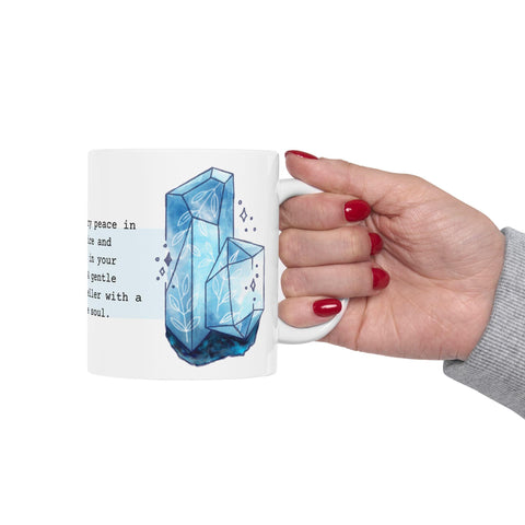 Hand with red nail polish holding white mug with blue crystal design and partial poetic text on white background