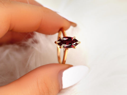 Close-up of hand holding a 14kt gold ring with a marquise ruby solitaire on a soft, light background