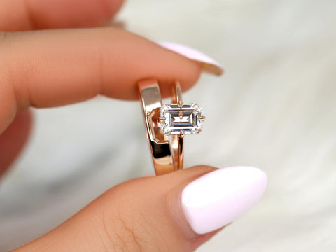 Hand holding two rose gold rings, one with an emerald cut moissanite solitaire and the other a polished band fine jewelry bridal set