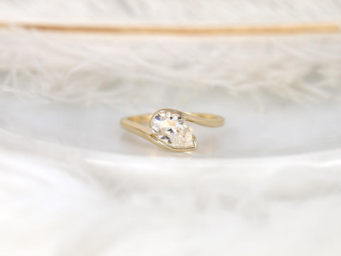 14kt gold ring with tilted pear-shaped moissanite solitaire stone on a delicate curved band displayed on white surface