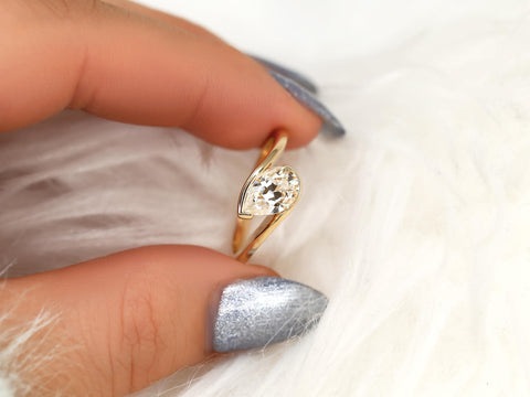 Close-up of a tilted pear-shaped moissanite set in a 14kt gold solitaire ring held between fingers with silver nails