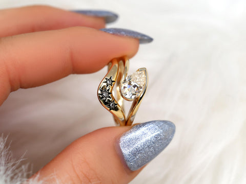 Gold bridal set with tilted pear moissanite solitaire and black star accents on polished bands held between fingers