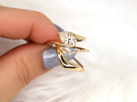 Close-up of a tilted pear-shaped moissanite engagement ring with matching curved 14kt gold wedding bands held by hand