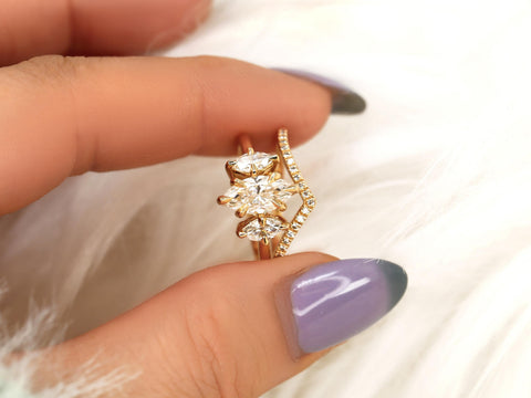 Hand holding a three-stone marquise moissanite bridal set with a curved diamond-accented 14kt gold band