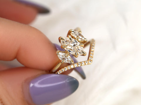 Hand holding a three-stone marquise moissanite bridal set with a delicate diamond-accented 14kt gold band