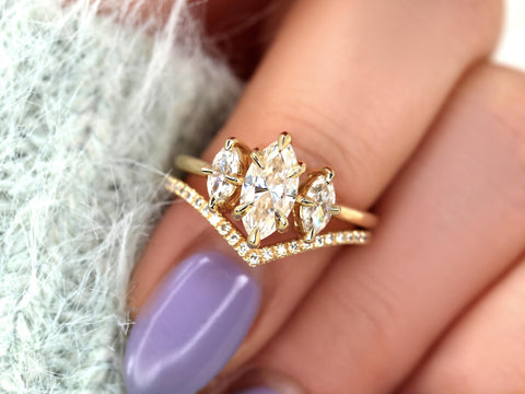 Close-up of a hand wearing a 14kt gold marquise moissanite three stone engagement ring with a curved diamond-accented wedding band