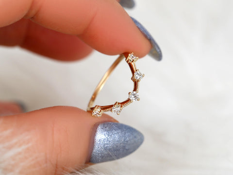 Delicate 14kt gold ring with five diamonds arranged in a curved, nesting design held between fingers