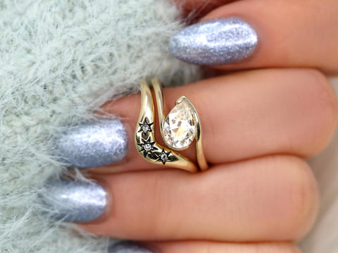 14kt gold ring set featuring a tilted pear moissanite stone and engraved star accents on band
